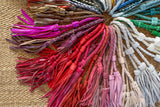 Colorful tassels arranged in a circular pattern on a textured surface.