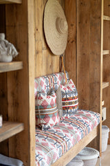 Patterned cushion on a wooden bench against a wooden wall with a hat hanging above.