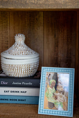 Decorative jar, books, and framed picture on a wooden shelf