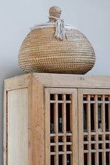 Woven basket with a lid on top of a wooden cabinet against a light gray wall.