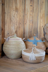 Three woven baskets with lids on a wooden surface against a wooden wall.