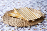 Yellow striped fabric on a woven mat with seashells on a floral tablecloth