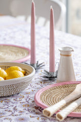 Table setting with pink candles, lemons, and decorative items on a floral tablecloth.