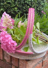 Woven basket with pink flowers and greenery on a brick surface
