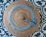 Woven hat with blue band and tassel on a patterned tile background