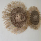 Two woven hats with fringes on a white wall