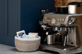 Espresso machine with a basket of coffee supplies on a kitchen counter.