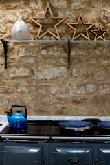 Blue teapot on a stove against a stone wall with decorative stars.