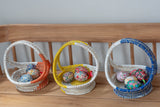 Three woven baskets with colorful eggs on a wooden surface