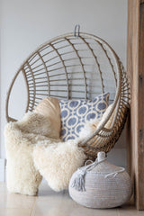 Wicker egg chair with cushions and a textured rug on a light wooden floor.