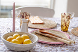 Handwoven natural NDONN placemat with pink leather trim styled on a table with lemons, wooden spoons and amber glasses.