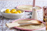 Handwoven placemats with pink leather edging on a table with lemons, ceramic jug and wooden spoon.