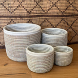 Set of four white handwoven open baskets with white leather trim in graduated sizes