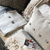 White linen cushions with African-sourced buttons, displayed on a sofa with decorative pillows, in a home setting.
