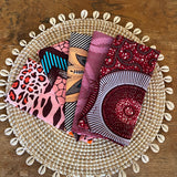Stack of patterned fabric pieces on a decorative woven plate with shell embellishments on a wooden surface.