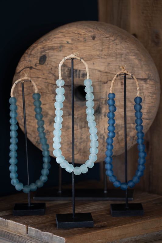Three beaded necklaces on stands against a wooden background