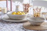 Dining table setting with lemons in a bowl, glasses, and cutlery on a patterned tablecloth.