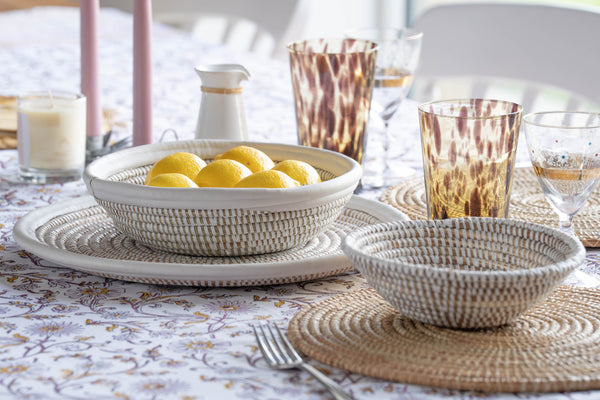Dining table setting with lemons in a bowl, glasses, and cutlery on a patterned tablecloth.