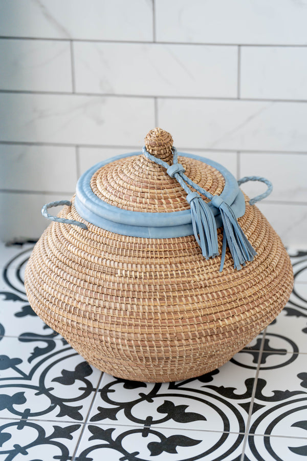 Woven basket with a blue lid and tassels on a tiled floor