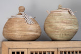 Two woven baskets with lids on a wooden surface against a gray background