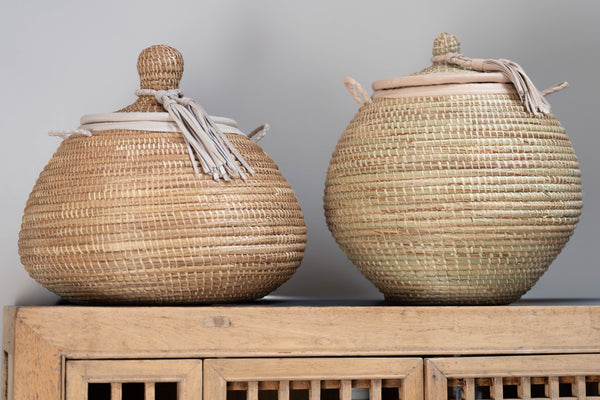 Two woven baskets with lids on a wooden surface against a gray background
