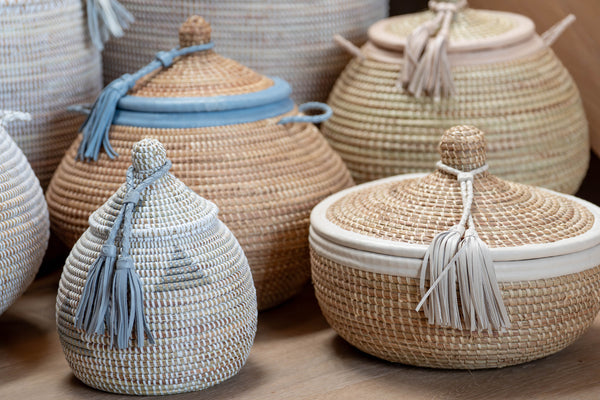 Woven baskets with lids and tassels on a wooden surface