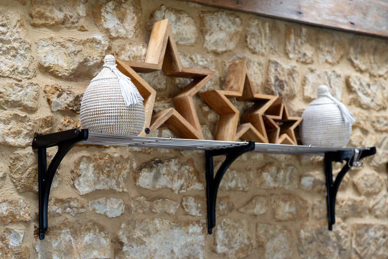 Decorative shelf with star-shaped wooden pieces and woven containers against a stone wall.