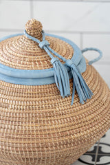 Close-up of natural handwoven lidded NDAR basket showing blue leather trim and tassel