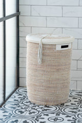 Tall flat-lidded white handwoven basket with leather trim, on patterned tiled floor
