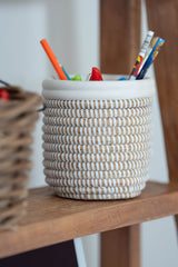White handwoven open basket with white leather trim used as a pen holder on a wooden shelf