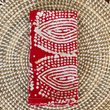 A pair of red and white patterned waxed cotton napkins with an eye design, laid out flat on a wicker surface.