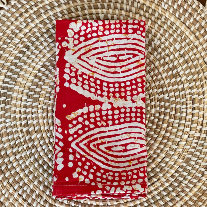 A pair of red and white patterned waxed cotton napkins with an eye design, laid out flat on a wicker surface.